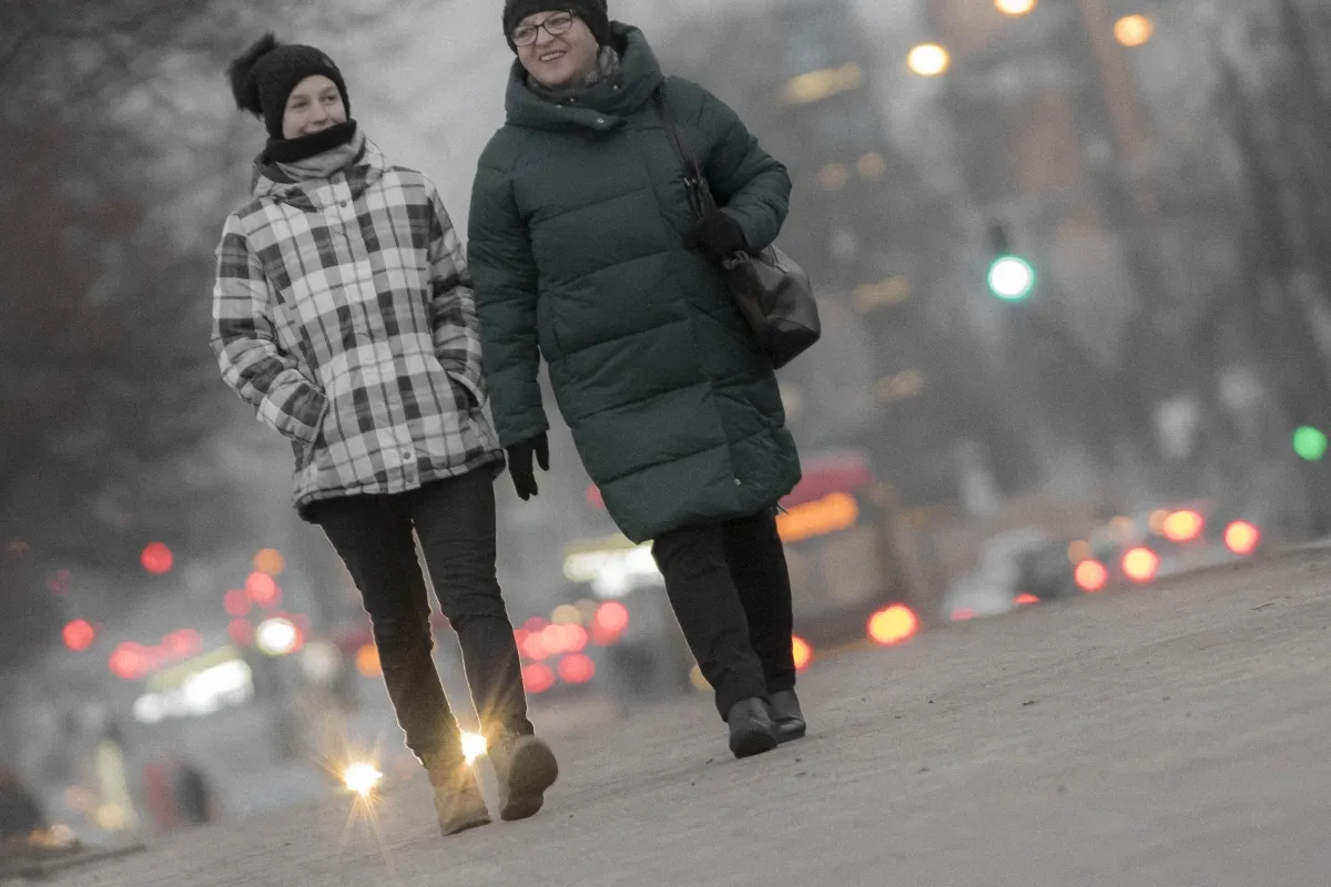 Woman and child walking toward the camera on a city street with blurred traffic lights